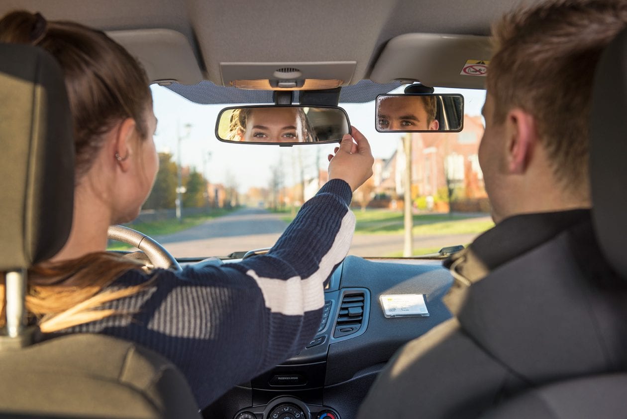 Leerling en instructeur kijken in de binnenspiegel van de auto