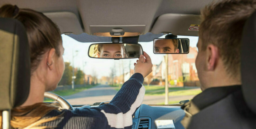 Leerling en instructeur kijken in de binnenspiegel van de auto